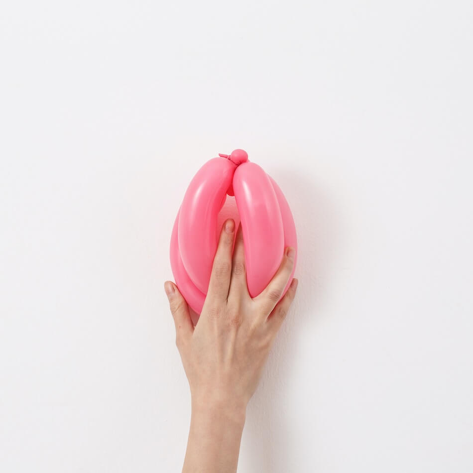 Hand, die einen rosa Luftballon in Form einer Vagina hält vor weißem Hintergrund